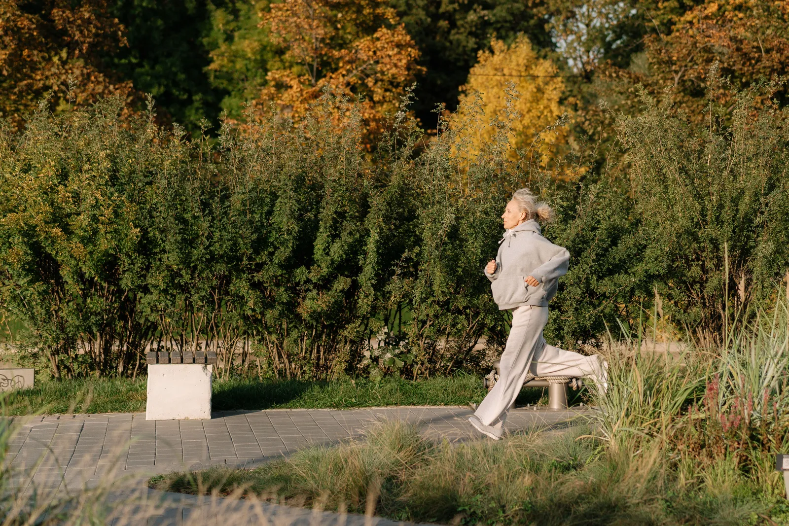 Older woman jogging on a park path among autumn trees